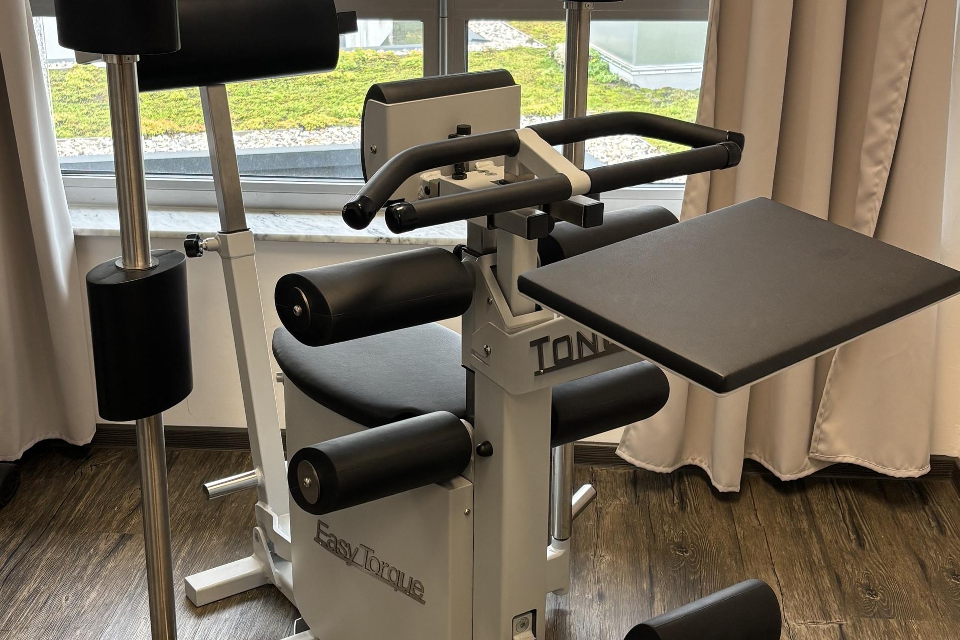 Fitnessgerät mit mehreren gepolsterten Hebeln, platziert in einem Raum mit Fenster und Holzfußboden.