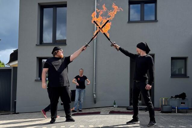 Auf dem Bild sieht man zwei junge Männer mit brennenden Feuerschwertern