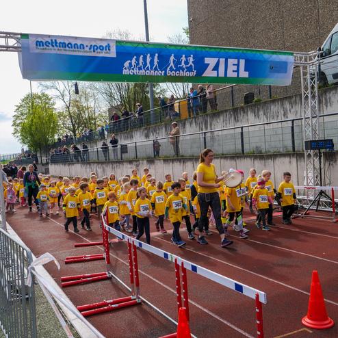 Gruppe von Kindern in gelben T-Shirts beim Ziel eines Laufwettbewerbs, angeführt von einer Frau mit einer Trommel.