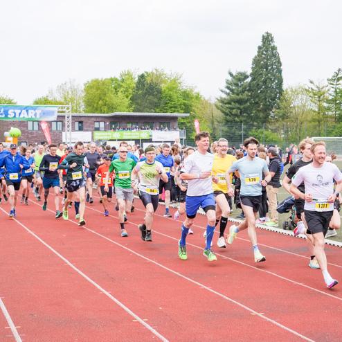 Große Gruppe von Läufern startet gleichzeitig auf einer roten Laufbahn unter einem "START"-Schild.