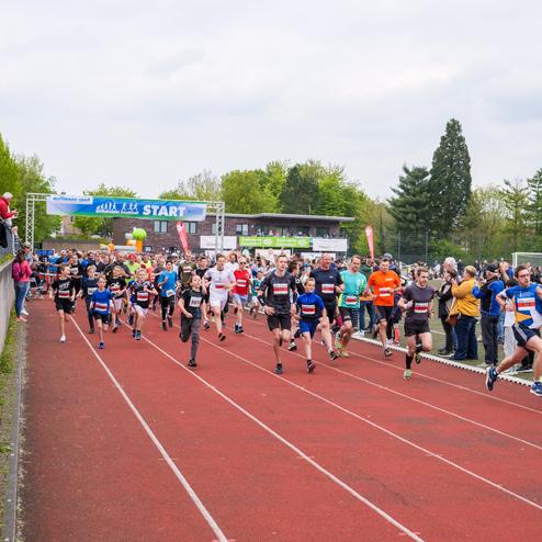 Startschuss für einen Laufwettbewerb mit zahlreichen Läufern auf der Rennbahn und Zuschauern am Rand.