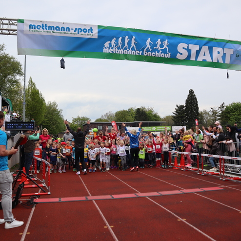 Startschuss beim Mettmanner Bachlauf: Kinder und Zuschauer jubeln vor der Startlinie mit Banner und Zeitmessung.
