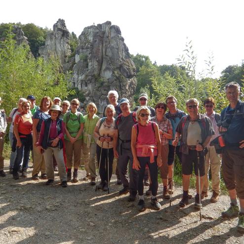 Gruppe von 18 Wanderern steht vor ungewöhnlichen Felsformationen in einer bewaldeten Umgebung.