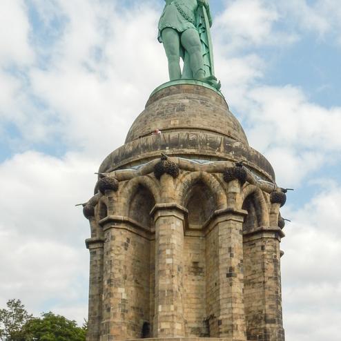 Gruppe von Wanderern posiert vor der Statue des Denkmal der Herrmann mit gehobenem Schwert auf einer steinernen Plattform.
