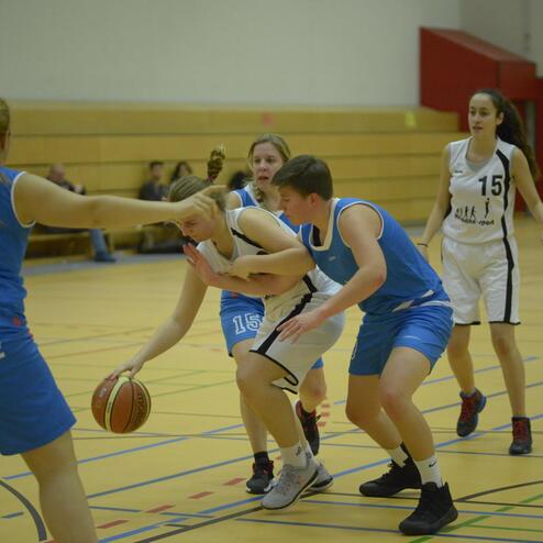 Basketballspiel: Zwei Spielerinnen kämpfen um den Ball, während ein Spieler der gegnerischen Mannschaft unterstützt.