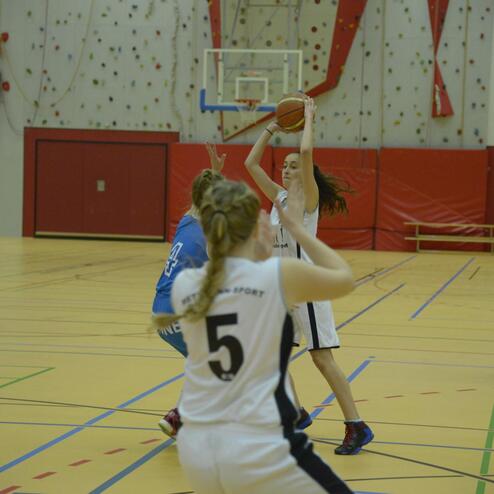 Basketballspiel: Eine Spielerin wirft den Ball, während zwei Gegnerinnen versuchen, ihn zu blockieren.
