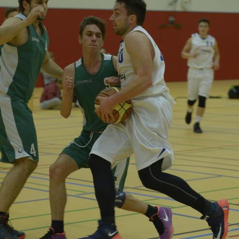 Zwei Basketballspieler in Aktion; einer mit Ball in der Hand, der andere versucht, ihn zu verteidigen.