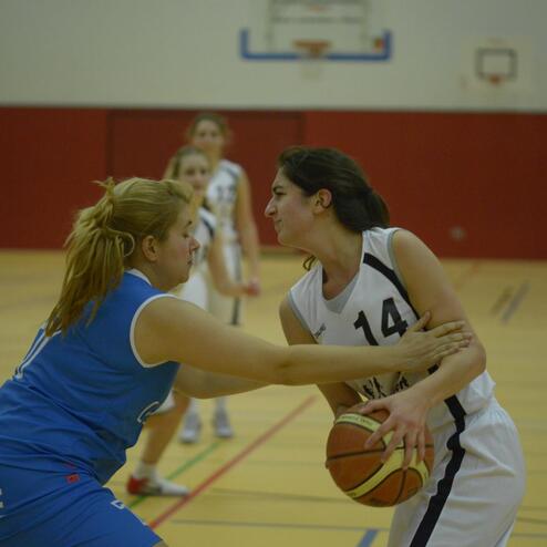 Zwei Basketballspielerinnen kämpfen um den Ball auf dem Spielfeld während eines Spiels in einer Sporthalle.