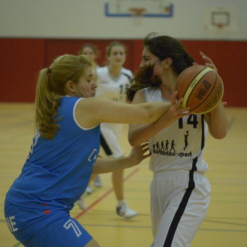Zwei Basketballspielerinnen kämpfen um den Ball in einer Sporthalle während eines Spiels.