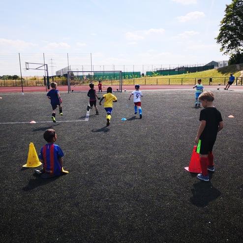 Gruppe von Kindern beim Fußballtraining auf einem Kunstrasenplatz, umringt von Trainingsmarkierungen und Toren.