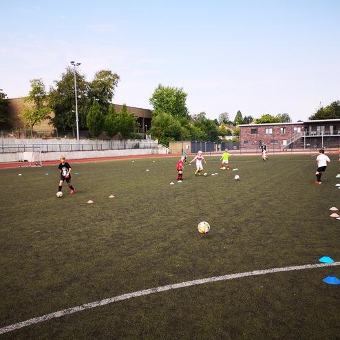 Kinder trainieren auf einem Fußballplatz mit Aufwärmübungen und Hütchen in verschiedenen Farben.