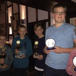 Fünf Jungen halten Pokale und Medaillen in einer festlichen Umgebung mit gedämpftem Licht.