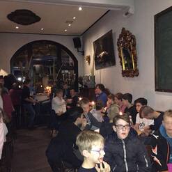 Gruppe von Jugendlichen in einem Raum, einige sitzen an Tischen, andere stehen, mit Kerzenlicht und dekorativen Elementen.