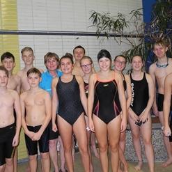 Gruppe von Schwimmern in Badeanzügen und Schwimmausrüstung, posierend am Rand des Schwimmbeckens.