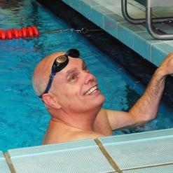 Schwimmer mit Sonnenbrille lächelt und hält sich am Beckenrand eines Schwimmbeckens fest.