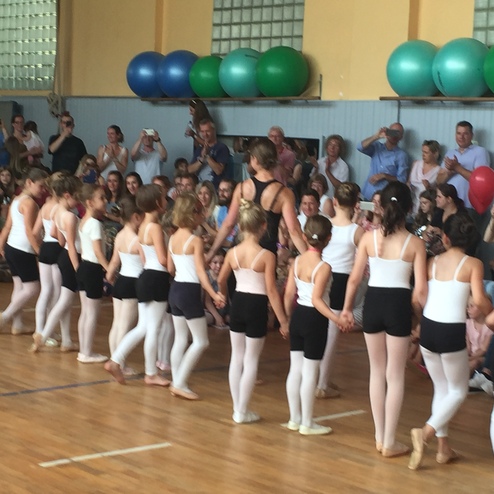 Gruppenvorstellung von Mädchen in Ballettkleidung, die auf einer Bühne vor einem Publikum zusammenstehen.