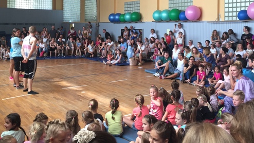 Vielzahl von Zuschauern in einem Sportbereich, während zwei Personen eine Vorführung durchführen. Bunte Gymnastikbälle im Hintergrund.