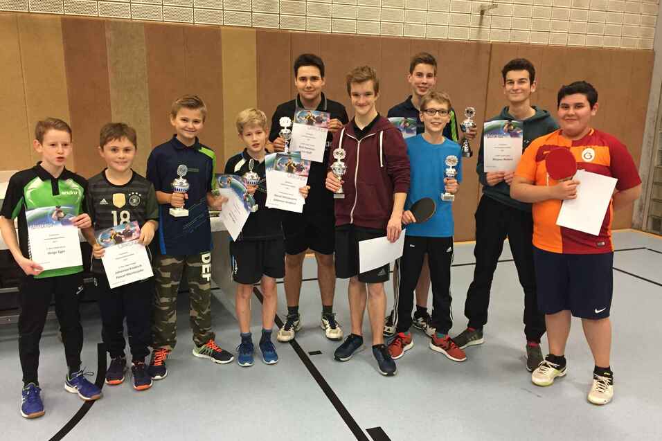 Gruppe von Jugendlichen mit Pokalen und Urkunden nach einem Tischtennisturnier in einem Sportraum.