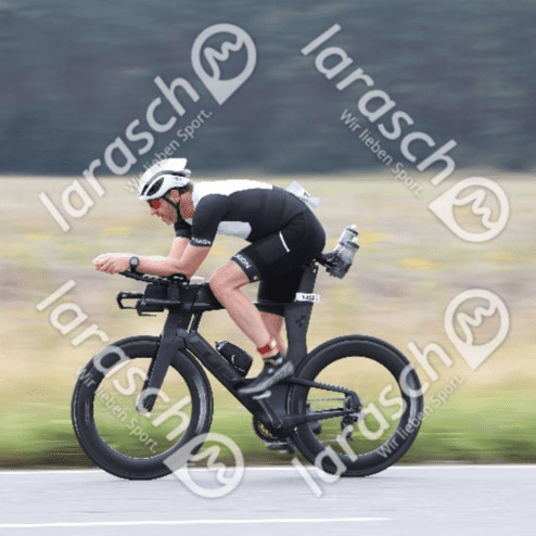 Radsportler in Aeroposition fährt auf einer Straße, mit sportlicher Ausrüstung und einem Flaschenhalter am Fahrrad.