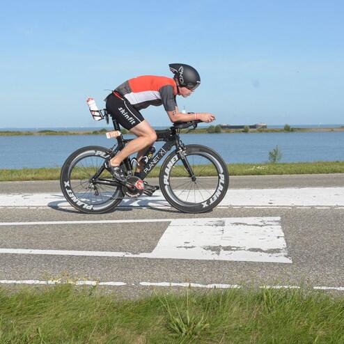 Sportler fährt auf einem Zeitfahrrad entlang einer Straße mit Wasser im Hintergrund. Schöne Wetterbedingungen.