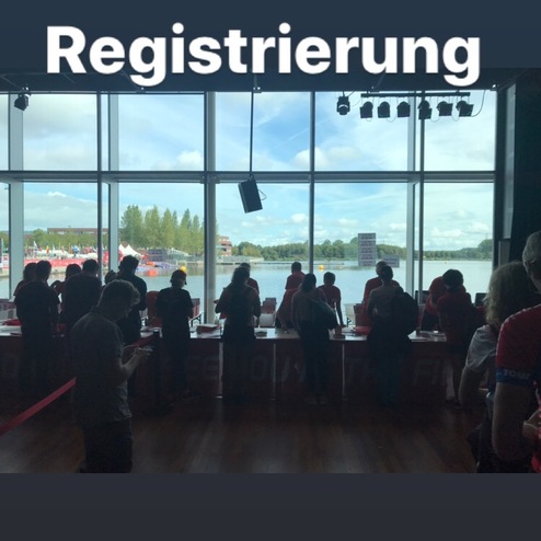 Menschen stehen an einem Registrierungsstand mit Blick auf einen See und bewölkten Himmel im Hintergrund.
