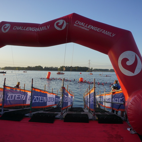 Startbogen des Triathlons über Wasser, mit Teilnehmern in Neoprenanzügen und roten Bojen erkennbar.