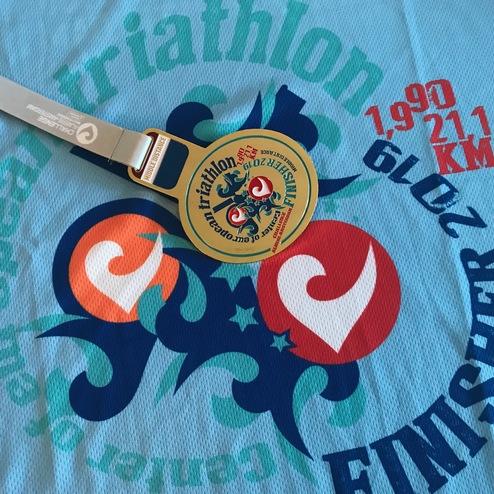 Finisher-Medaille und Triathlon-Shirt mit Aufdruck „1,9 KM Schwimmen, 21,1 KM Laufen, 2019“.