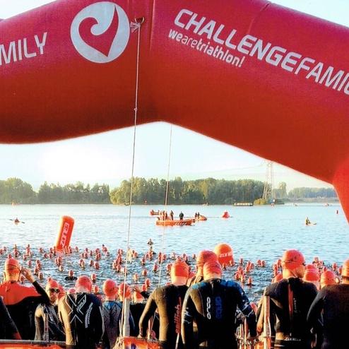 Teilnehmer in roten Schwimmkappen stehen am Ufer eines Gewässers, um an einem Triathlon teilzunehmen.