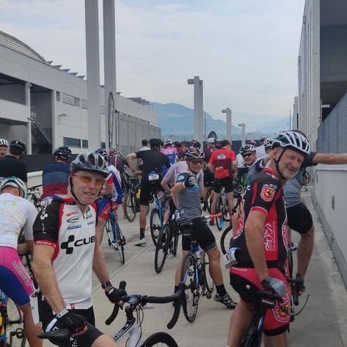 Gruppierung von Radfahrern in Sportkleidung, die auf einem Gehweg vor einem Gebäude warten.