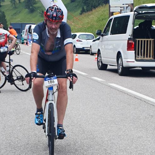 Radfahrer mit Nummer 186 auf Straße, im Hintergrund ein Startbogen und weitere Teilnehmer beim Wettkampf.