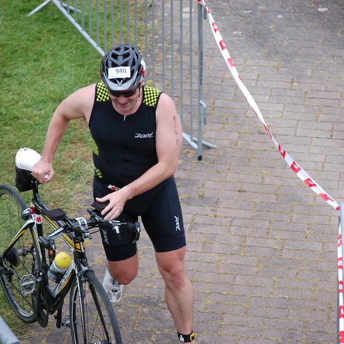 Athlet in Sportanzug schiebt sein Rennrad über einen gefliesten Weg während eines Wettkampfs.