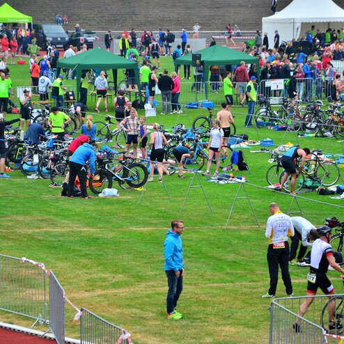 Triathlon-Teilnehmer bereiten ihre Fahrräder und Ausrüstung auf einer Wiese vor einer Sportveranstaltung vor.