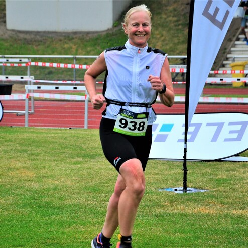Läuferin in sportlicher Kleidung läuft auf einer Wiese, mit Nummernschild 938 und banners im Hintergrund.