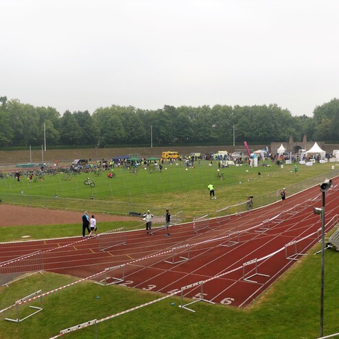 Überblick über ein Sportfeld mit Radfahrern, Zuschauern und Zelten, umgeben von einer Laufbahn.