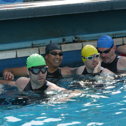 Fünf Schwimmer in Badekappen stehen in einem Schwimmbecken und unterhalten sich.