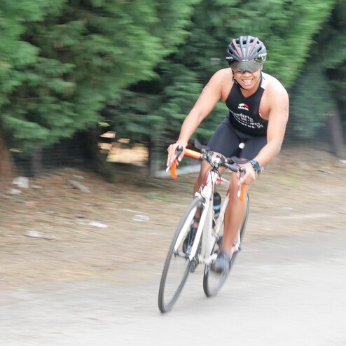 Radfahrer in Sportkleidung sprintet auf einem schmalen Weg, umgeben von grünen Bäumen.
