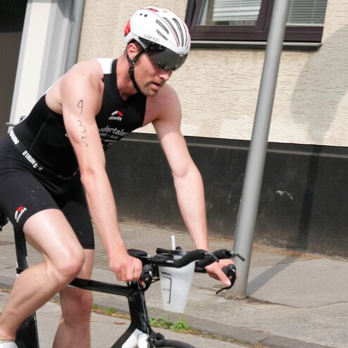 Radfahrer in sportlicher Kleidung fährt auf einer Straße vorbei, mit einem Getränkhalter am Fahrrad.