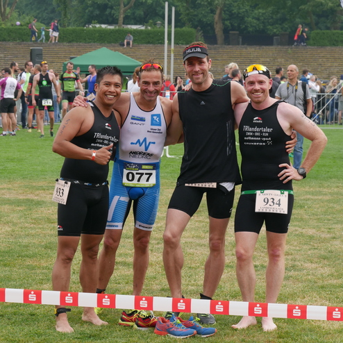Vier Männer in Sportbekleidung stehen lächelnd nach einem Wettkampf zusammen auf einer Rasenfläche.