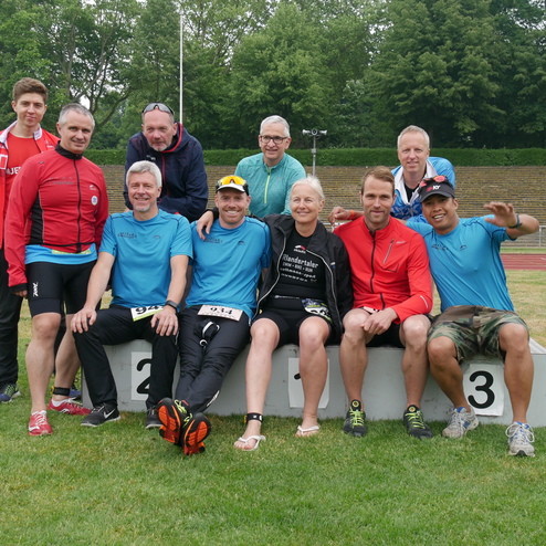 Gruppe von Sportlern in wasserdichten Shirts, posierend auf einem Siegerpodest auf einem Stadionrasen.