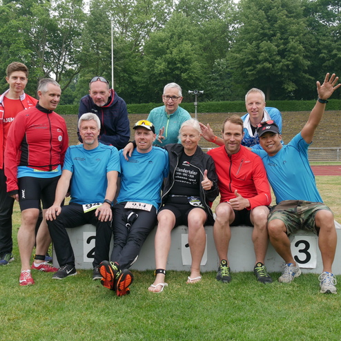 Gruppenschnappschuss von zehn Personen in Sportbekleidung auf einem Podest auf einem Sportplatz, lächelnd und posierend.