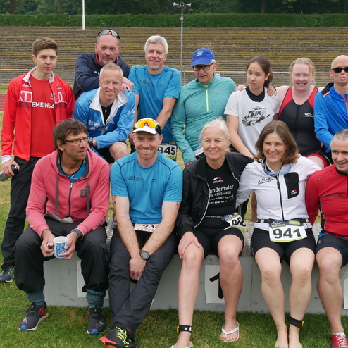 Gruppe von Sportlern in Laufkleidung posiert auf einem Siegerpodest bei einer Veranstaltung im Freien.
