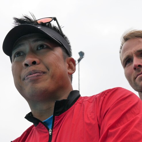 Porträt zweier Sportler in roten Jacken, einer mit Kappe, beide blicken konzentriert in die Ferne.