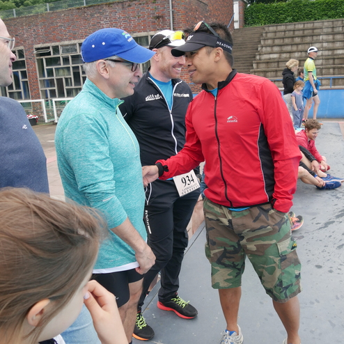 Gruppe von Männern in Sportkleidung unterhält sich, während ein Mädchen im Vordergrund zusieht. Sportveranstaltung im Freien.