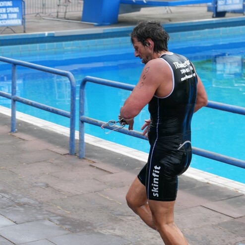 Triathlet in schwarzem Anzug läuft mit Schwimmbrille zur Poolkante nach dem Schwimmen. Nasses Gleis im Vordergrund.