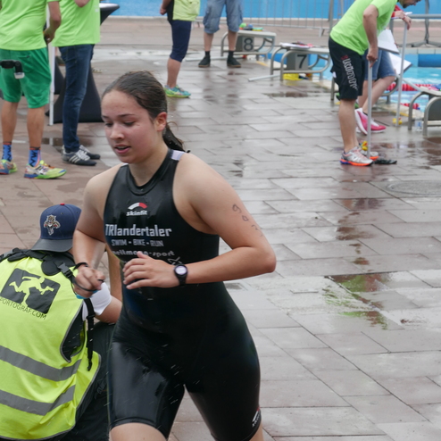 Junge Frau in einem schwarzen Triathlonanzug läuft während eines Wettkampfs an einem Schwimmbecken vorbei.