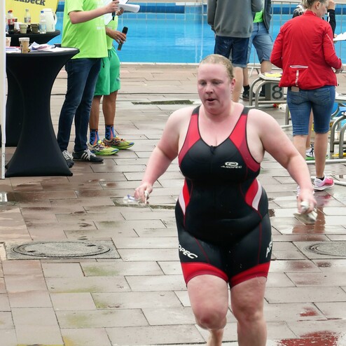 Frau in einem schwarzen Schwimmanzug läuft barfuß nach einem Wettkampf neben einem Schwimmbecken und Zuschauern.