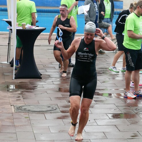 Teilnehmerin an einem Schwimmwettbewerb zieht beim Verlassen des Beckens ihre Badekappe ab, umgeben von anderen Aktiven.