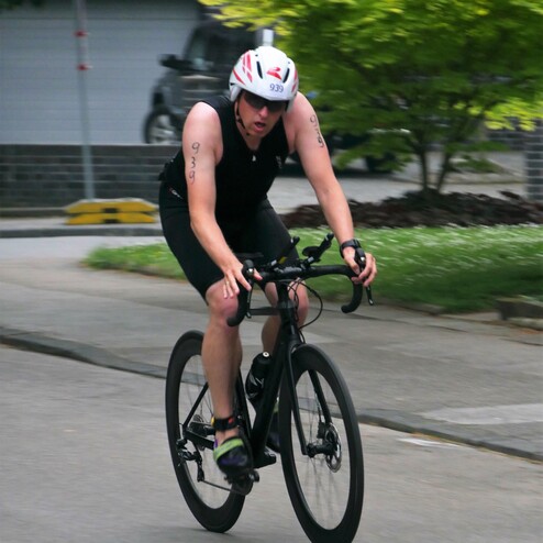Radfahrer in sportlicher Kleidung fährt auf einer Straße, trägt einen Helm mit der Nummer 939 und hat einen entschlossenen Ausdruck.