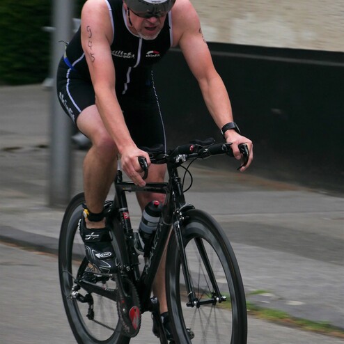 Sportler in Triathlonanzug fährt auf einem Rennrad während eines Wettkampfs auf der Straße.