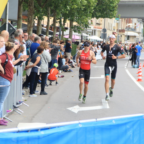 Zwei Athleten in Wettkampfkleidung laufen entlang einer Zuschauerlinie bei einem Triathlon-Event.